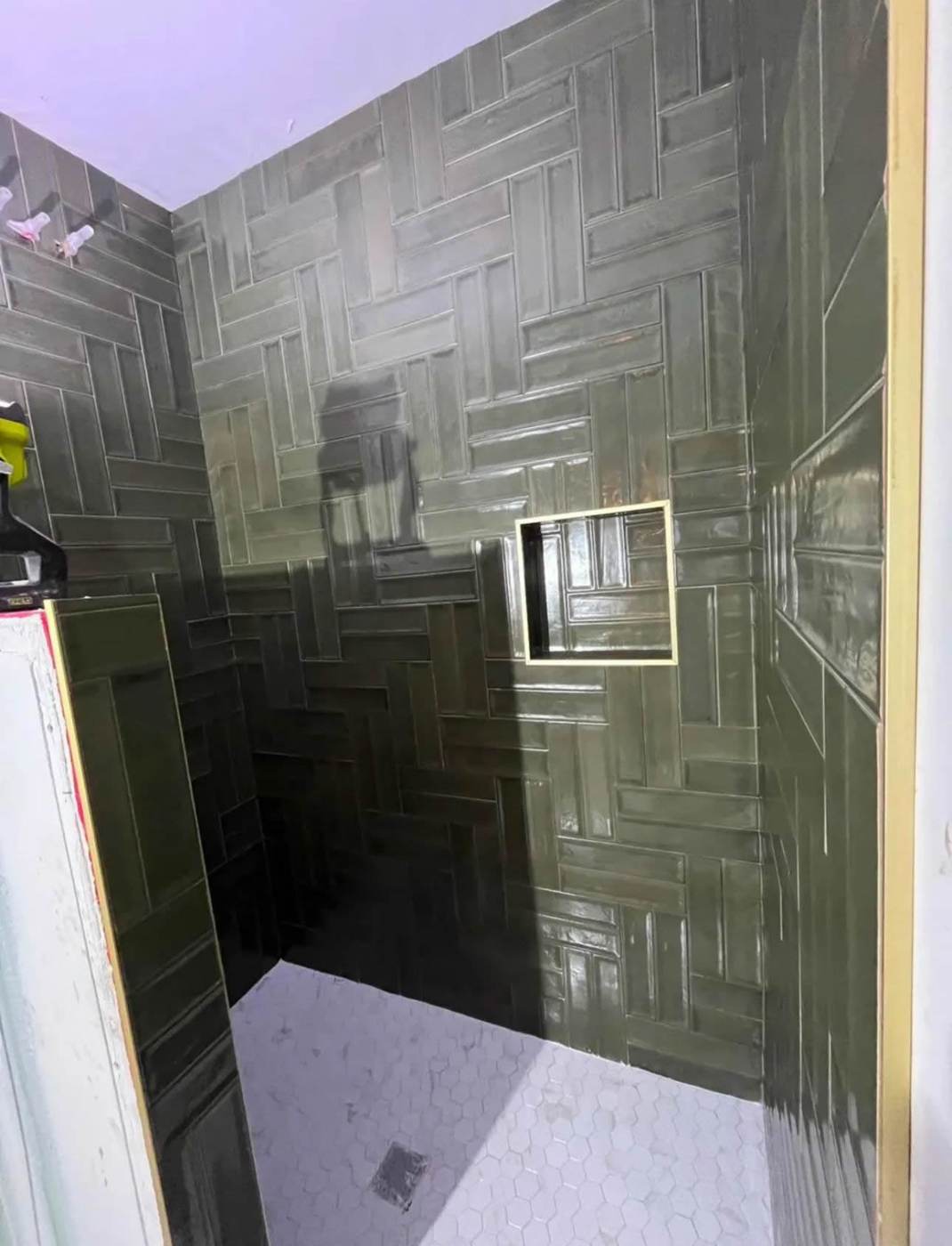 Dark green herringbone tile on the shower walls with a recessed niche.