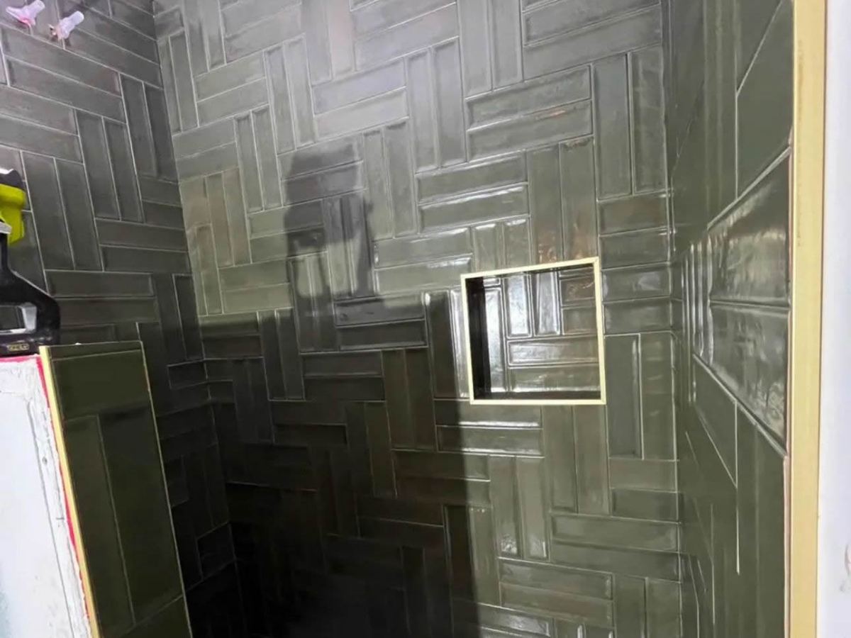 Dark green herringbone tile on a walk-in shower wall with a recessed niche
